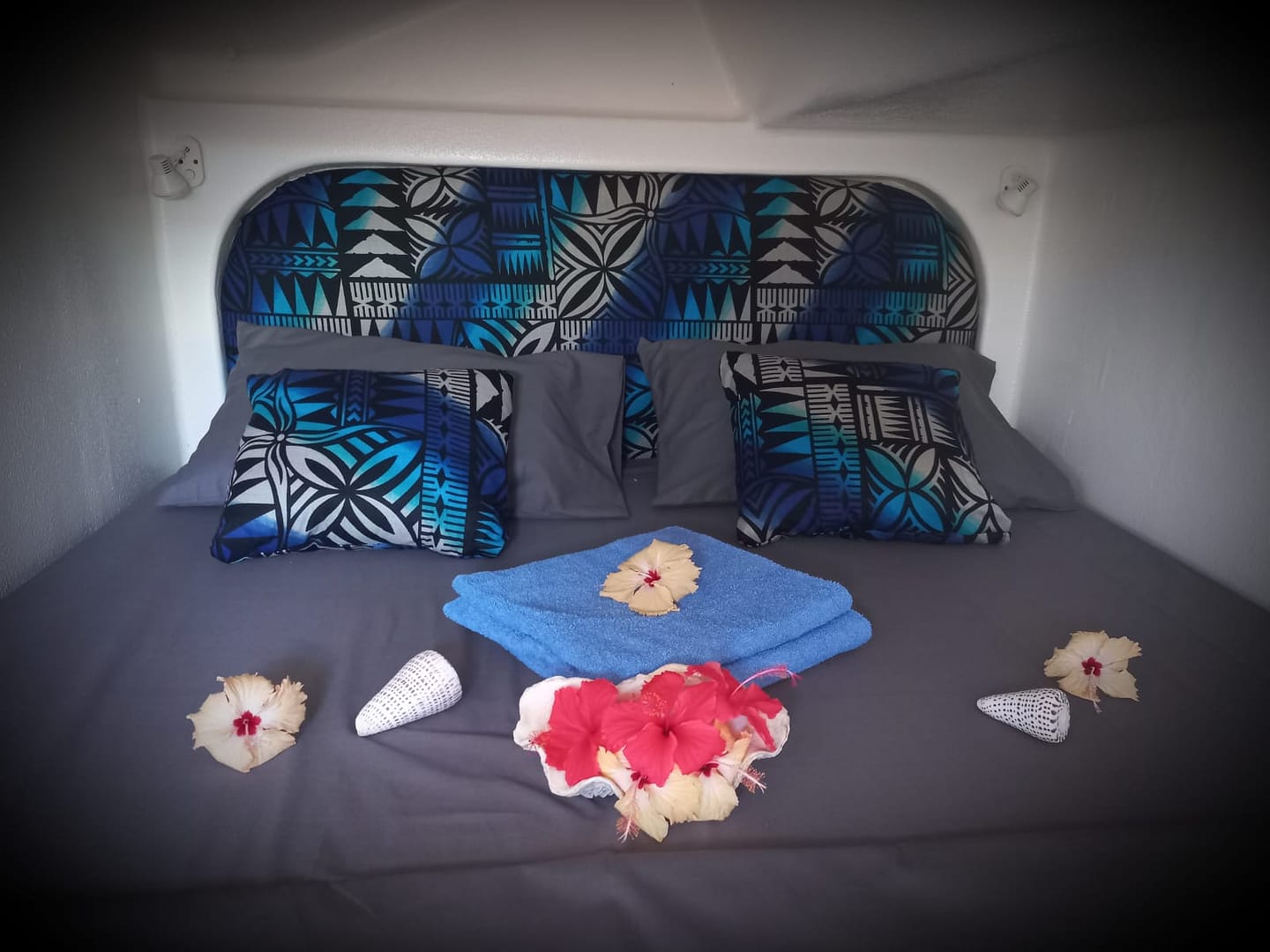 A neatly made bed with a patterned headboard and matching pillows, decorated with flowers and small woven conical objects, with a blue towel in the center.