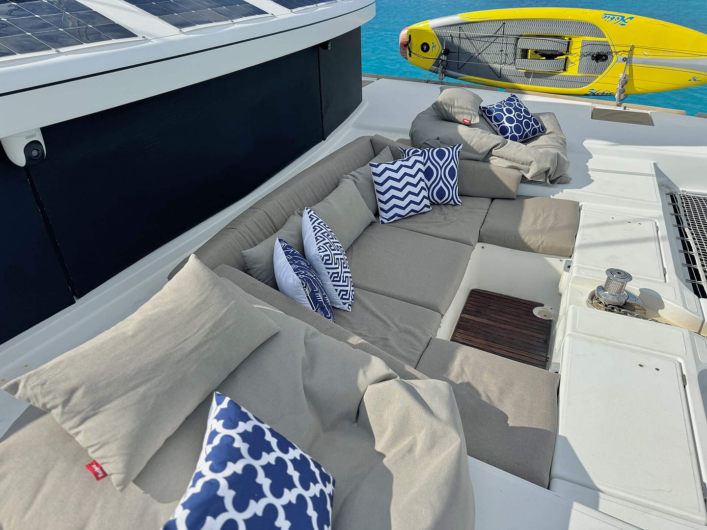 A daytime view of a yacht's outdoor seating area with beige cushions and blue-and-white patterned pillows, overlooking the water with a yellow kayak nearby.