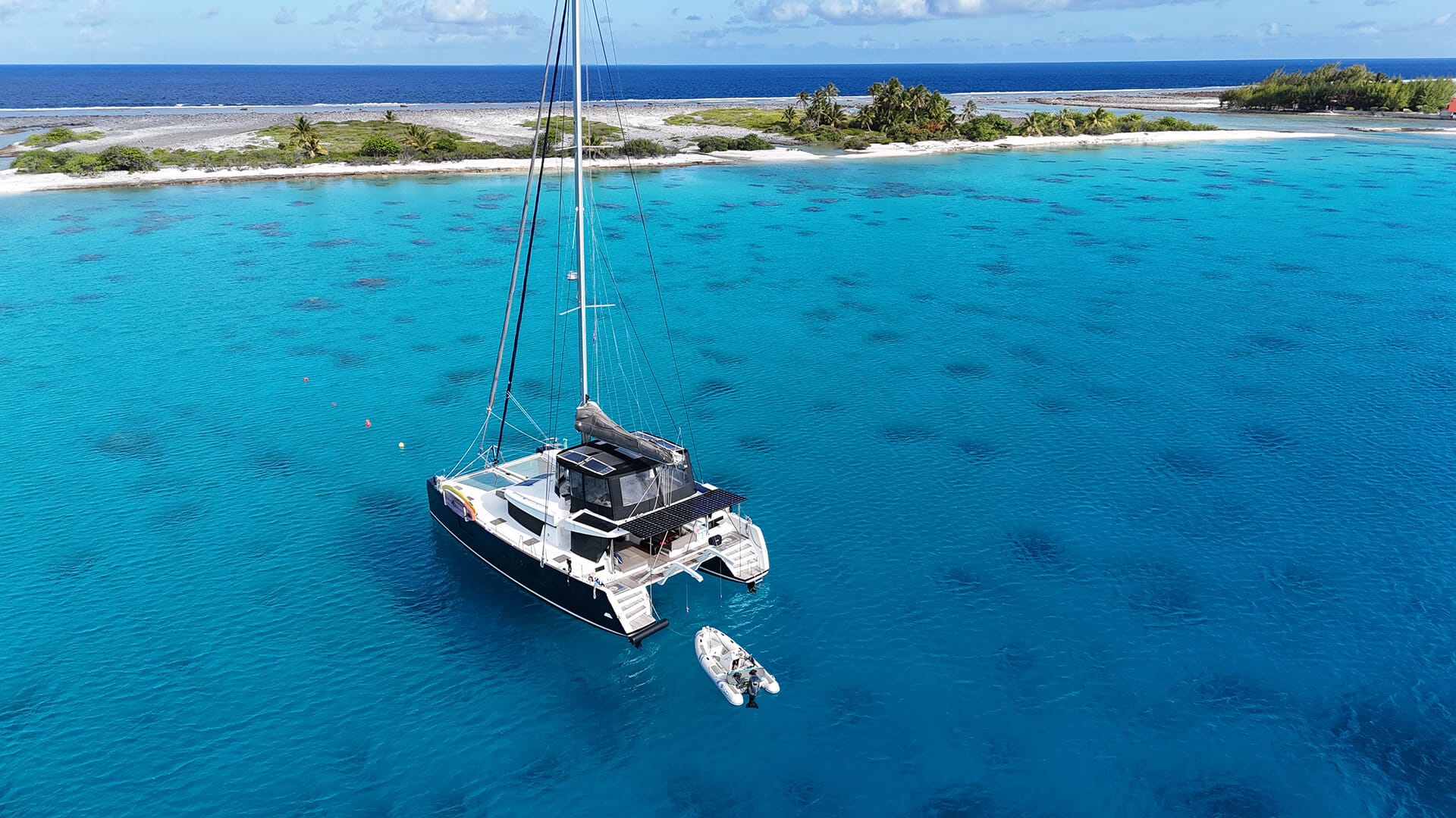 A sailboat anchored in clear blue ocean waters near a sandy island with green vegetation and palm trees.